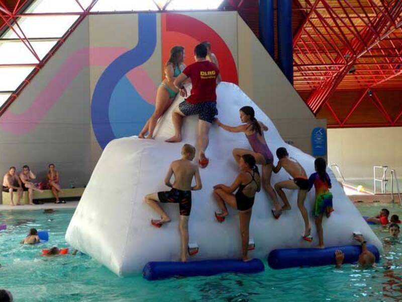 Kinder klettern auf ein aufblasbares Spielelement, das im Wasserbecken schwimmt.