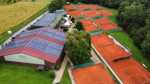 Das Clubhaus mit Solarpaneelen steht neben dicht gereihten Sandplätzen, Wege verbinden Anlage und Spielfelder.