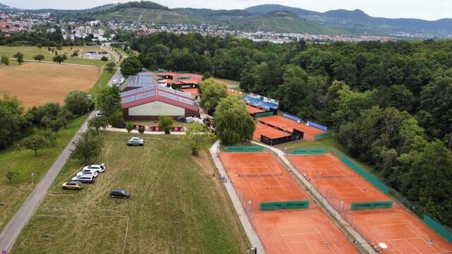 Blick von oben auf Tennisplätze am Waldrand, dahinter eine Stadt und Hügel in der Ferne.