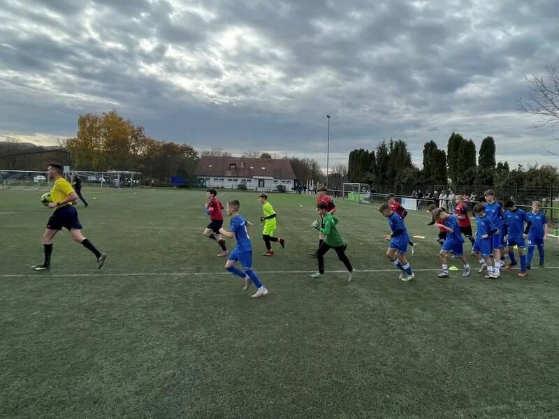 Eine Gruppe von jungen Fußballspielern in blauen und roten Trikots läuft gemeinsam mit einem Schiedsrichter auf einen Fußballplatz.