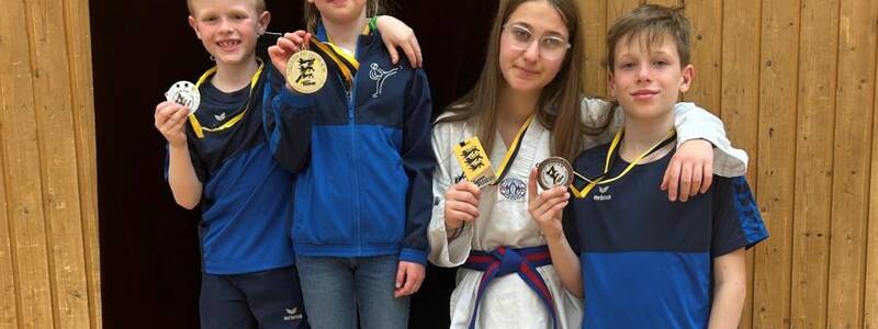 Vier Kinder stehen lächelnd vor einem Banner der Taekwondo Union Baden-Württemberg und zeigen stolz ihre Medaillen.