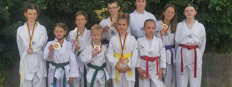 Eine Gruppe von Kindern und Jugendlichen steht in Karateanzügen draußen und hält Medaillen um den Hals.