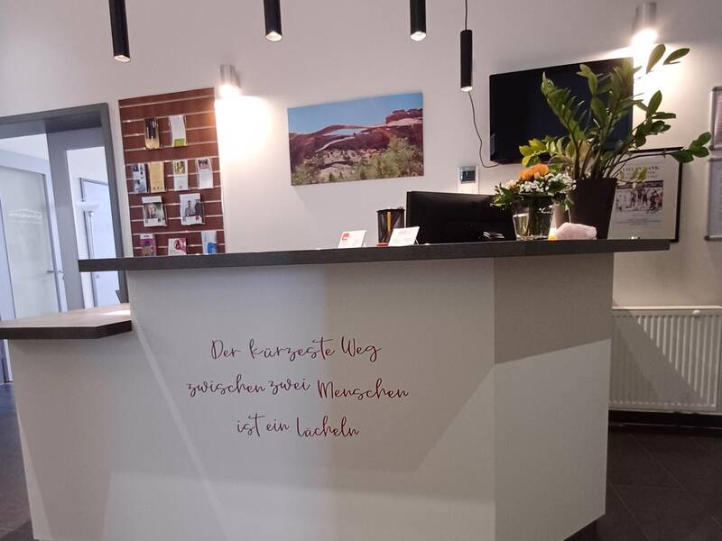 Der Empfangstresen in einem modernen Raum ist mit einer Pflanze, Fotos und der Aufschrift "Der kürzeste Weg zwischen zwei Menschen ist ein Lächeln" dekoriert.